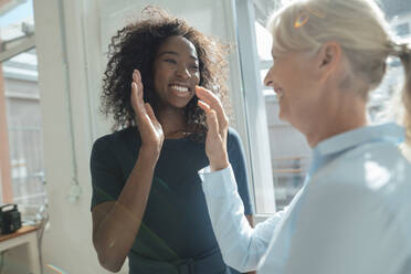 Smiling businesswoman giving high-five to colleague in office - KNSF09391