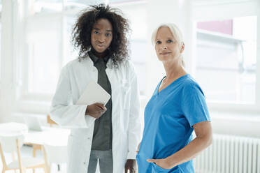 Krankenschwester mit Händen in den Taschen, die neben einer Ärztin mit einem Tablet-PC steht - KNSF09408