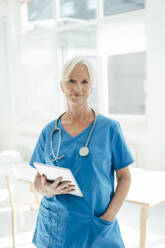 Smiling female doctor holding tablet PC standing with hand in pocket - KNSF09411