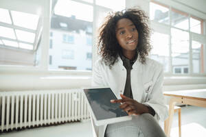 Female doctor pointing at tablet PC sitting on chair - KNSF09434