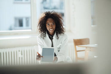 Smiling female doctor with curly hair pointing at tablet PC - KNSF09435