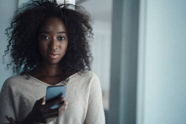 Junge Frau mit lockigem Haar, die ein Mobiltelefon hält - KNSF09450
