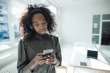 Young woman holding mobile phone listening music through wireless headphones - KNSF09469