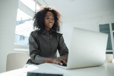 Businesswoman using laptop at desk in office - KNSF09477