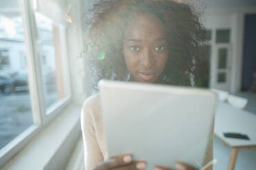 Junge Geschäftsfrau mit lockigem Haar hält Tablet-PC im Büro - KNSF09485
