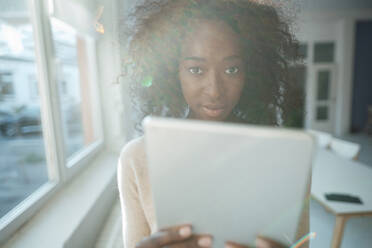 Young businesswoman with curly hair holding tablet PC in office - KNSF09485