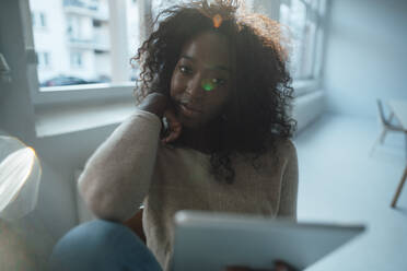 Young businesswoman with curly hair holding tablet PC in office - KNSF09493