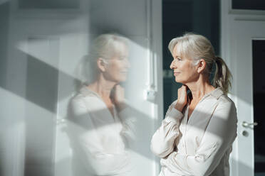 Smiling businesswoman looking through window in office - KNSF09517