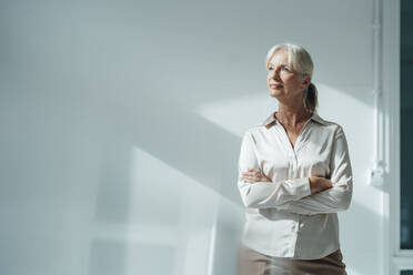 Senior businesswoman standing with arms crossed in office - KNSF09519