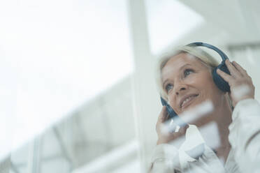 Smiling senior woman listening music seen through glass - KNSF09535