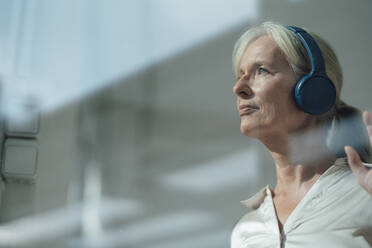 Smiling senior woman listening music through wireless headphones - KNSF09539
