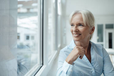 Happy senior businesswoman looking through window in office - KNSF09545