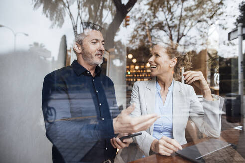 Lächelnder Geschäftsmann im Gespräch mit Geschäftsfrau in Café durch Glas gesehen - JOSEF10813