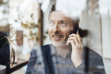 Lächelnder Geschäftsmann, der mit seinem Handy telefoniert, gesehen durch Glas - JOSEF10832