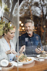 Geschäftsfrau mit Geschäftsmann, der ein Mobiltelefon hält, beim Mittagessen in einem Cafe - JOSEF10838