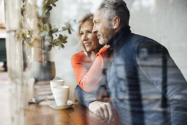 Smiling couple sitting in cafe seen through glass - JOSEF10844