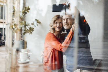 Smiling man with woman taking selfie through smart phone in cafe - JOSEF10853