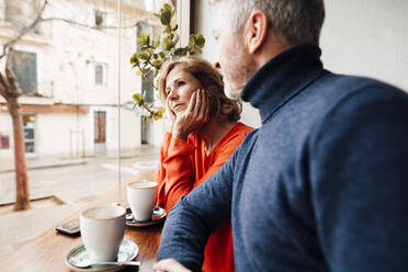 Man looking at woman sitting with head in hands at cafe - JOSEF10863