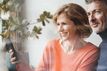 Smiling man standing by woman using smart phone in cafe - JOSEF10865