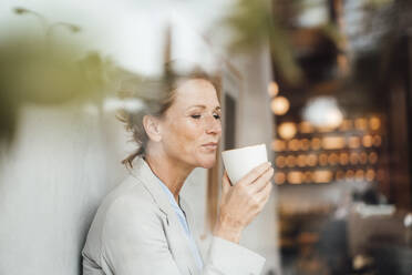Businesswoman having coffee in cafe seen through glass - JOSEF10885