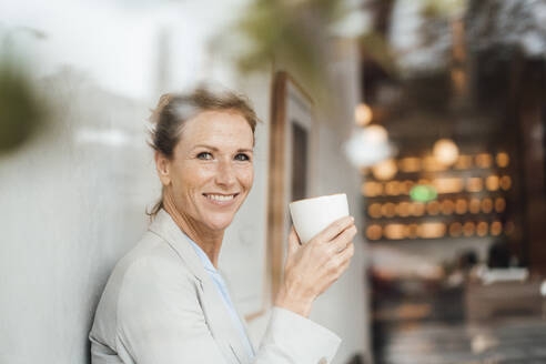 Happy businesswoman holding coffee cup in cafe - JOSEF10886