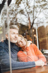 Smiling man embracing woman sitting in cafe seen through glass - JOSEF10893