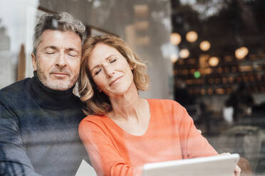 Smiling couple with eyes closed sitting in cafe seen through glass - JOSEF10898