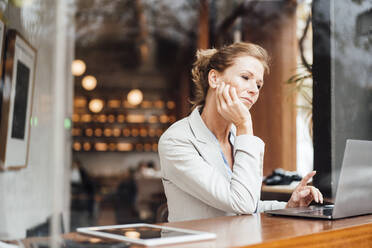 Businesswoman with head in hand looking at laptop seen through glass - JOSEF10918