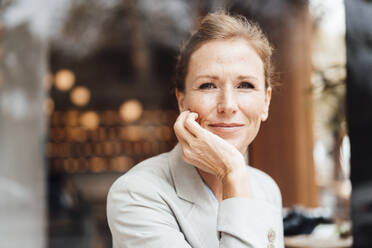 Smiling businesswoman with head in hand at cafe - JOSEF10919