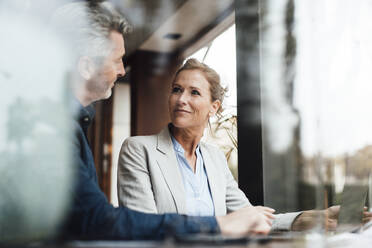 Smiling businesswoman with businessman in cafe seen through glass - JOSEF10922