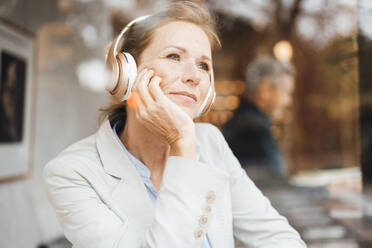 Lächelnde Geschäftsfrau hört Musik über drahtlose Kopfhörer in einem Café - JOSEF10929