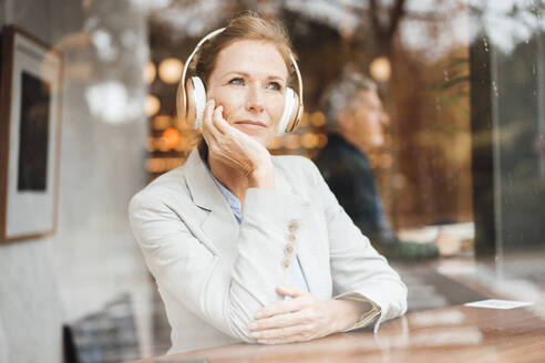 Geschäftsfrau mit dem Kopf in der Hand hört Musik über drahtlose Kopfhörer in einem Cafe - JOSEF10930