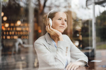 Businesswoman listening music through wireless headphones in cafe - JOSEF10933