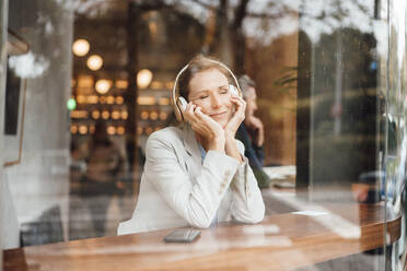 Lächelnde Geschäftsfrau mit geschlossenen Augen hört Musik in einem Café durch Glas gesehen - JOSEF10936