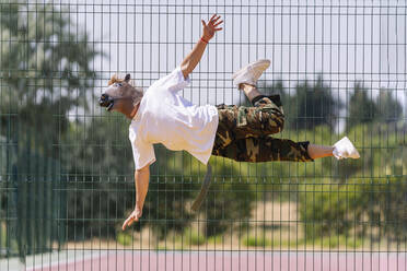 Tänzerin mit Tiermaske, die sich an einem sonnigen Tag vor einem Zaun dreht - OCMF02514