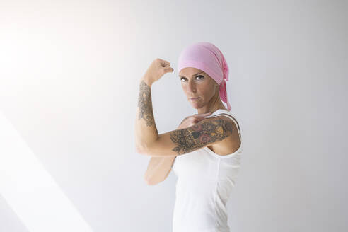Frau mit rosafarbenem Schal, die vor einer Wand ihre Muskeln anspannt - MTBF01241