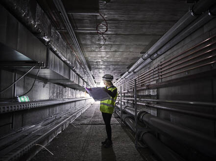 Young engineer looking at blueprint standing in tunnel - CVF02043