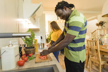 Lächelnder Mann, der mit seiner Freundin in der Küche zu Hause Tomaten schneidet - OSF00296