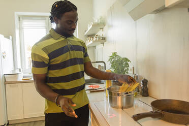 Young man putting uncooked spaghetti in cooking pot at kitchen - OSF00299