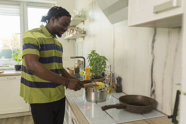 Smiling man cooking spaghetti in cooking pot at kitchen - OSF00300