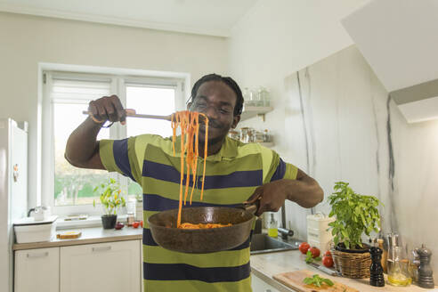 Lächelnder Mann hält eine Pfanne mit Spaghetti in der Küche - OSF00304