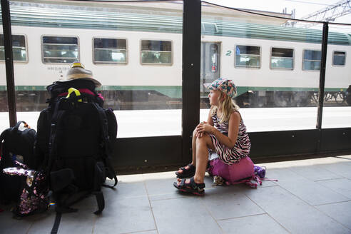 Mädchen sitzt auf Tasche am Bahnhof - FOLF11530