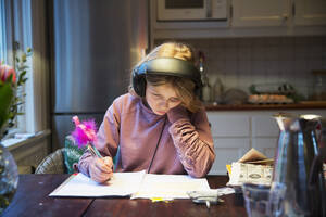 Mädchen mit Kopfhörern studiert am Küchentisch - FOLF11543