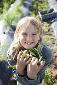 Lächelndes Mädchen hält Bohnen im Garten - FOLF11553