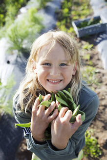 Smiling girl holding beans in garden - FOLF11553