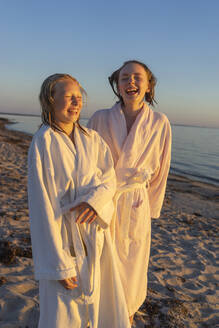 Lachende Mädchen in Bademänteln am Strand bei Sonnenuntergang - FOLF11577