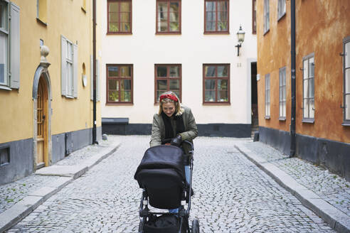 Frau zu Fuß mit Kinderwagen auf der Straße - FOLF11580