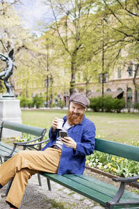 Lächelnder Mann mit Smartphone auf einer Parkbank - FOLF11587