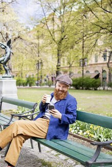 Smiling man using smart phone on park bench - FOLF11587