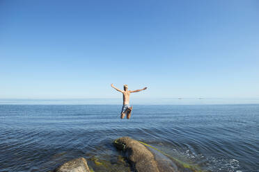 Junger Mann springt von einem Felsen am Meer - FOLF11598